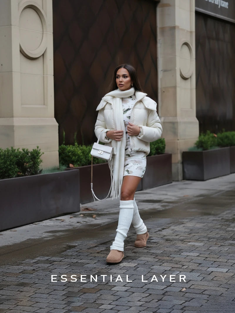 Woman in a white coat walking on a city street with 'Essential Layers' branding.