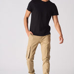 A man wearing slim fit beige cotton cargo pants with a black t-shirt and trainers.