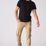 A man wearing slim fit beige cotton cargo pants with a black t-shirt and trainers.