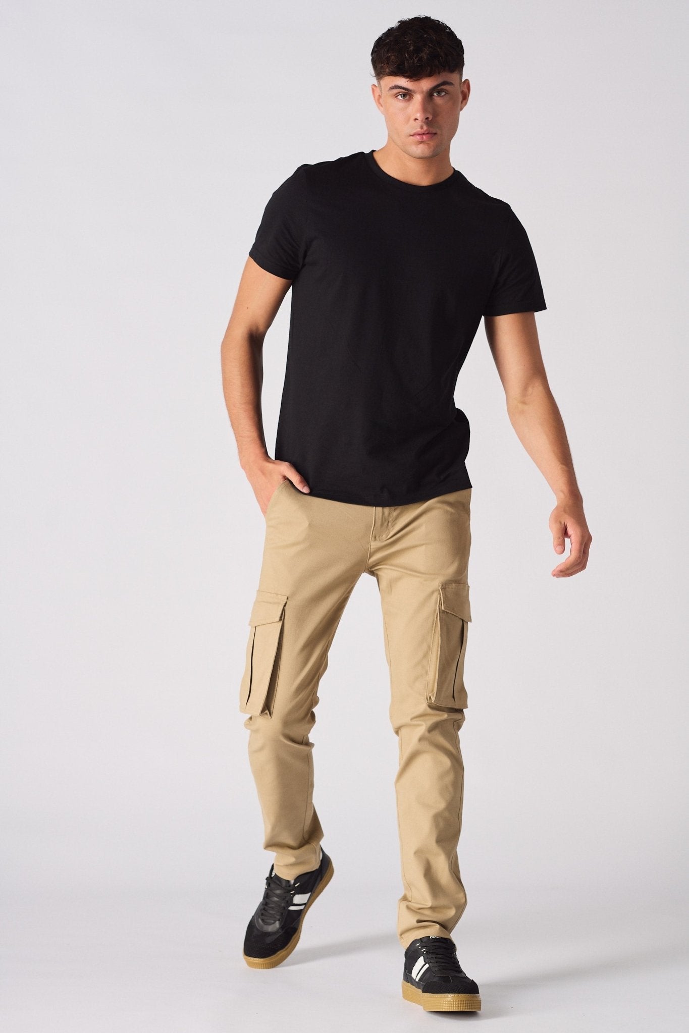 A man wearing slim fit beige cotton cargo pants with a black t-shirt and trainers.