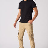 Full length front view of a man styled in beige cotton cargo pants and a black tee.