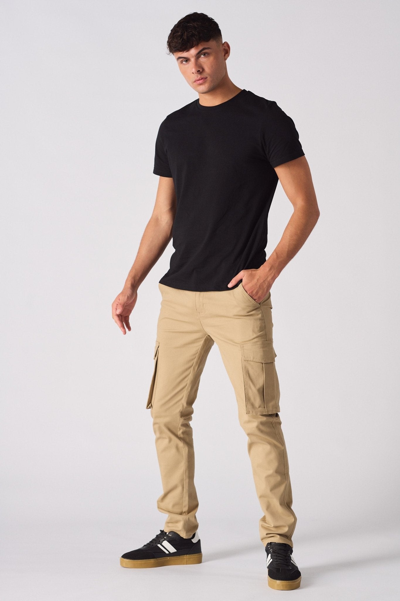 Full length front view of a man styled in beige cotton cargo pants and a black tee.