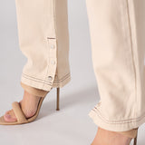Beige high-heeled sandals worn with beige pants on a light gray background