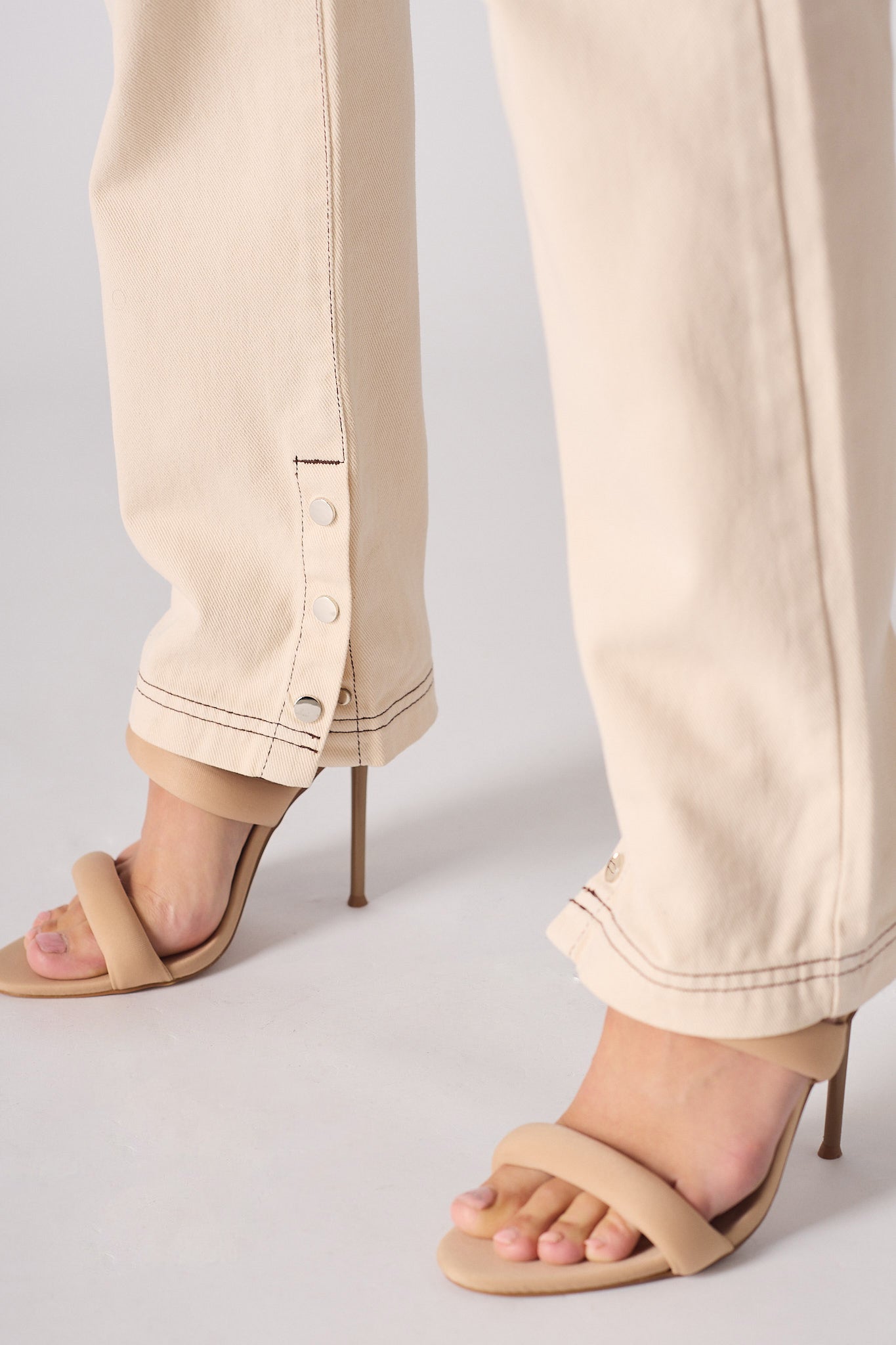 Beige high-heeled sandals worn with beige pants on a light gray background