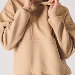 A woman adjusting the popper neck detail on a soft beige hoodie