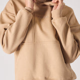 A woman adjusting the popper neck detail on a soft beige hoodie