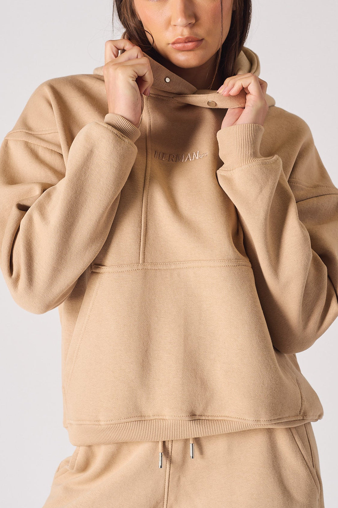 A woman adjusting the popper neck detail on a soft beige hoodie