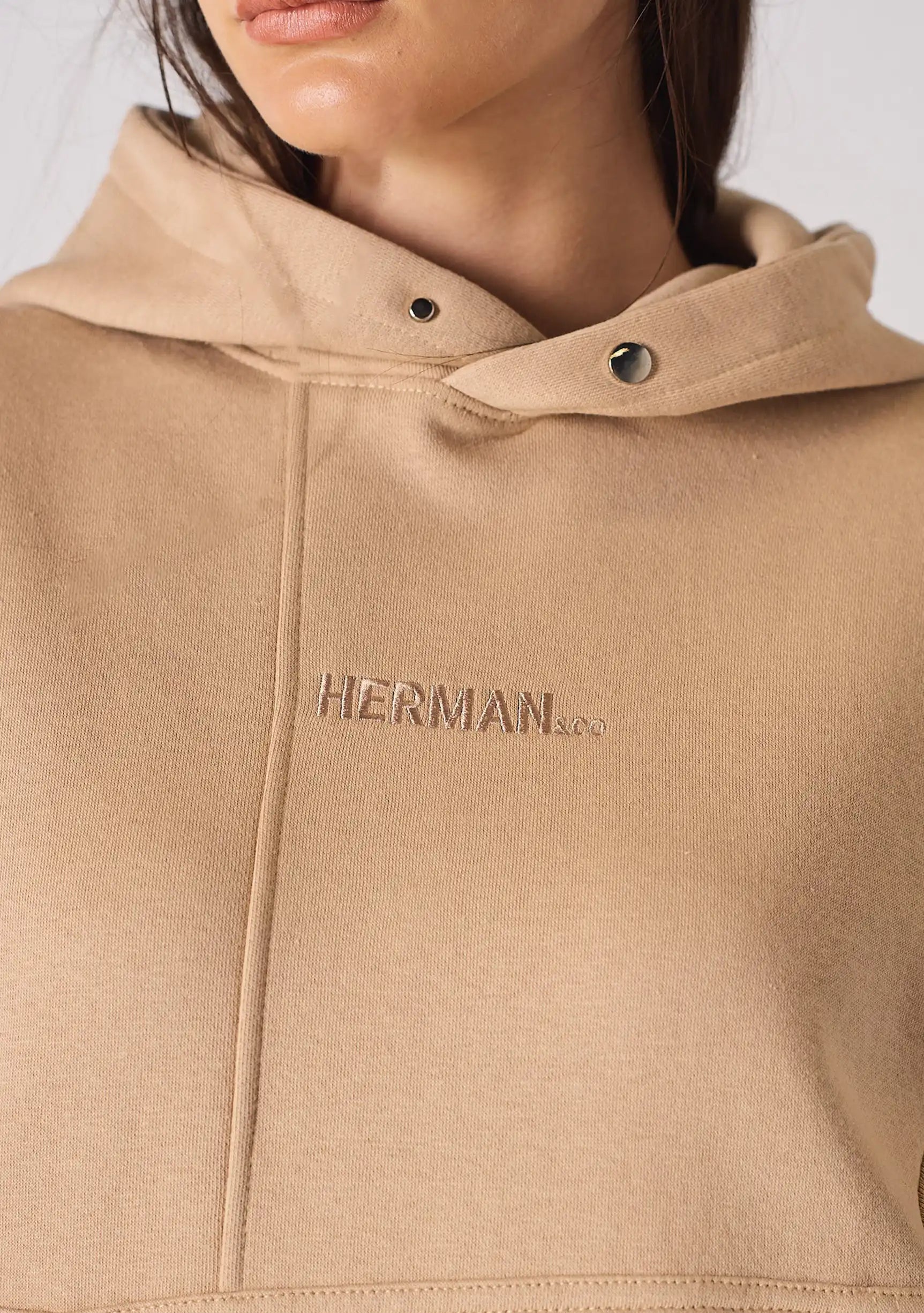 Close up of the tonal embroidered insignia on a beige hoodie for women