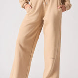 A front view of a woman wearing beige wide leg joggers with hands in her pockets