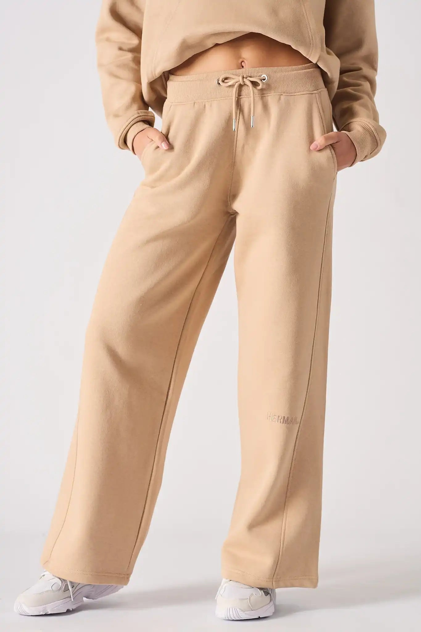 A front view of a woman wearing beige wide leg joggers with hands in her pockets