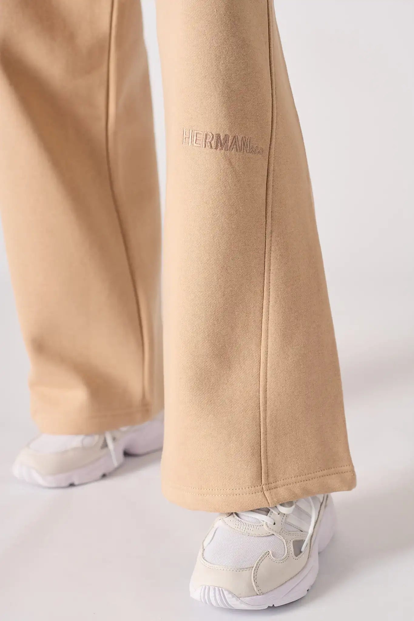 Detailed view of the discreet tonal logo on the beige wide leg joggers