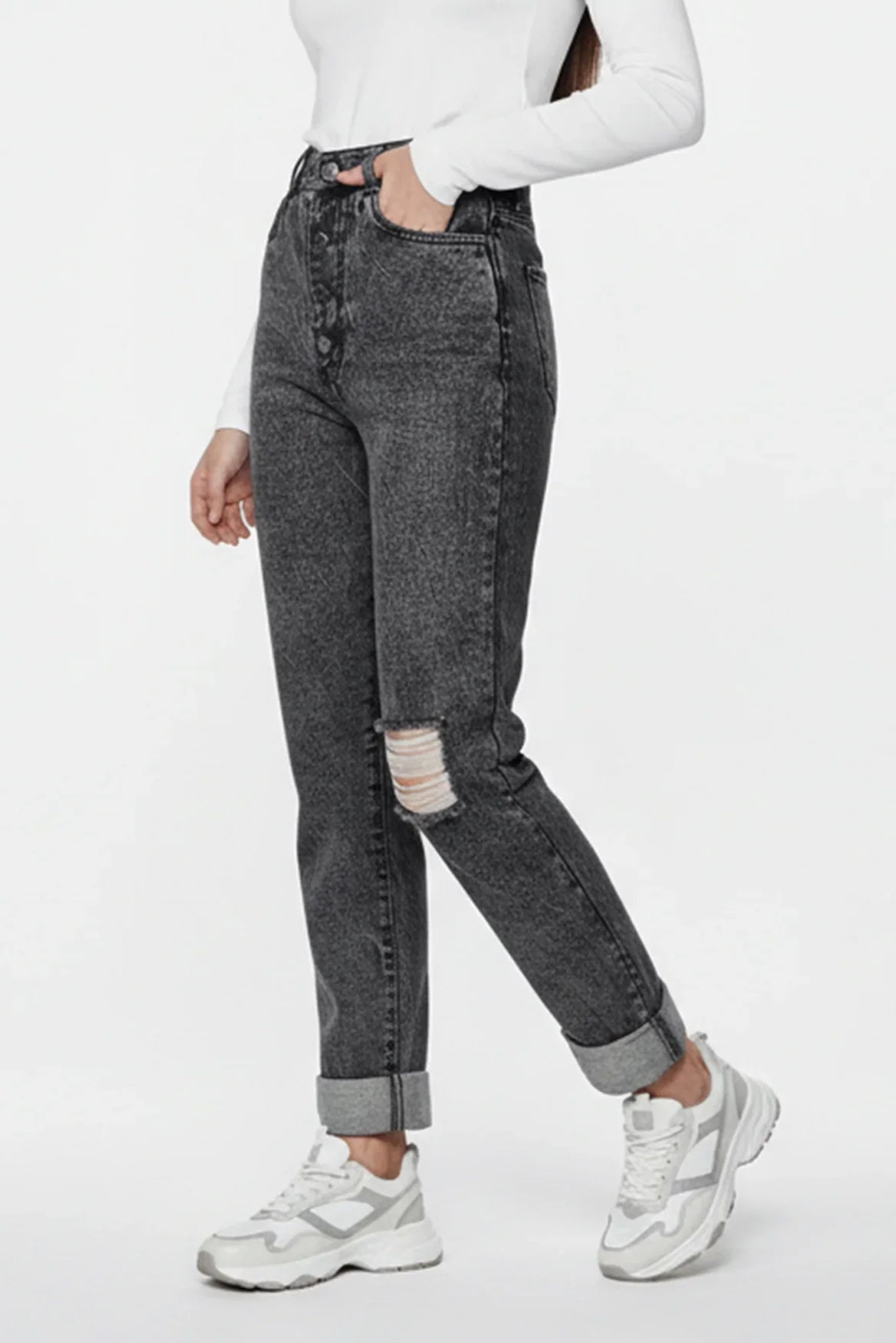 Person wearing black acid-wash jeans with a white top and white sneakers on a white background