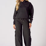 Full length front view of a model styling black wide leg cargo joggers and a hoodie
