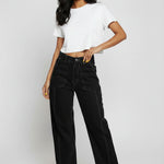 Full body view of model standing in black wide-leg jeans featuring white contrast stitching and utility pockets.