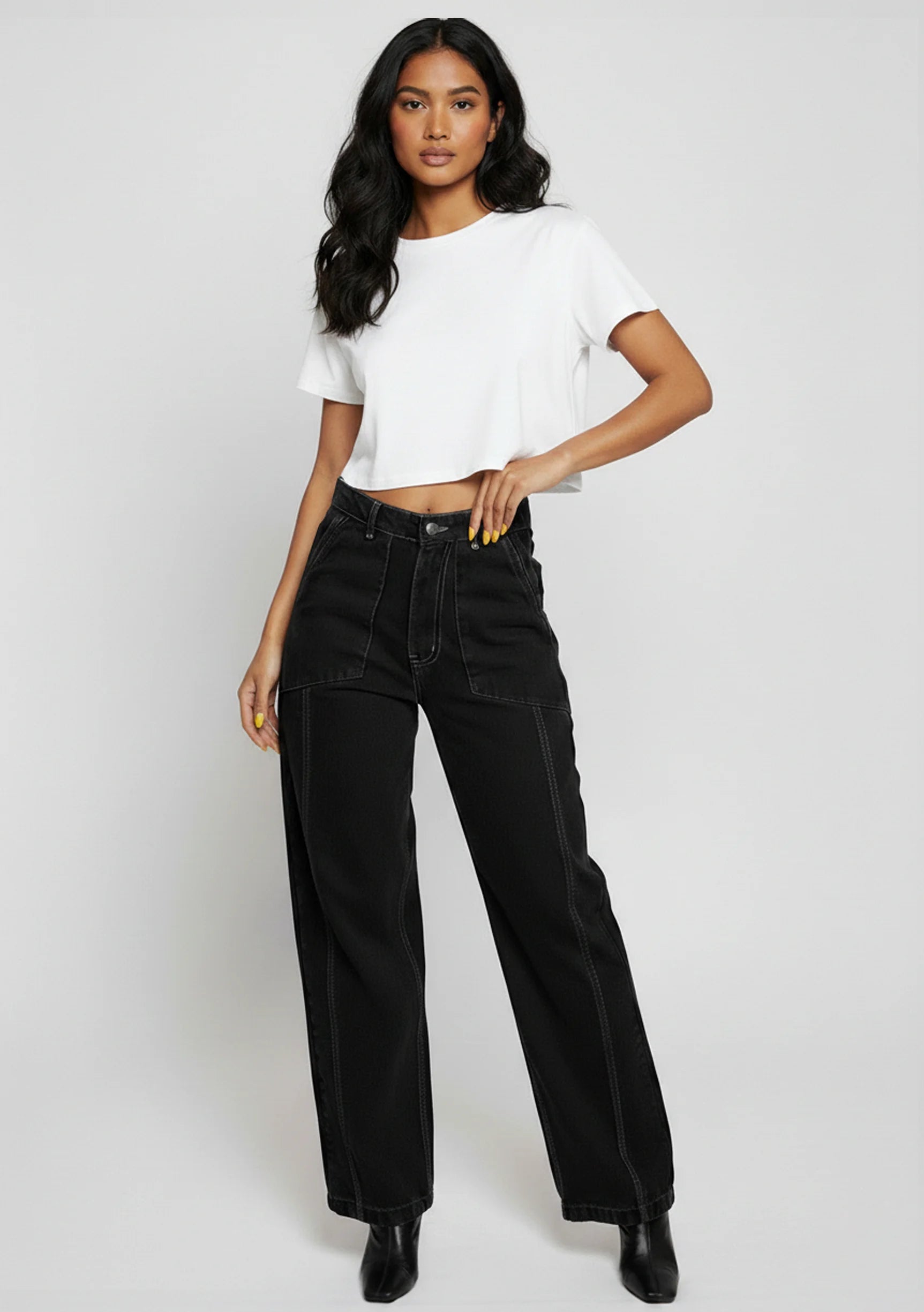 Full body view of model standing in black wide-leg jeans featuring white contrast stitching and utility pockets.