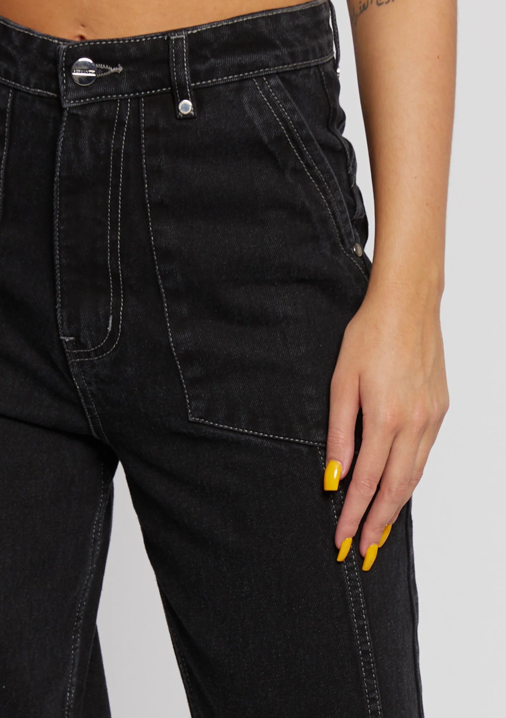 Macro shot of black denim waist showing fabric texture, button closure, and white stitching.