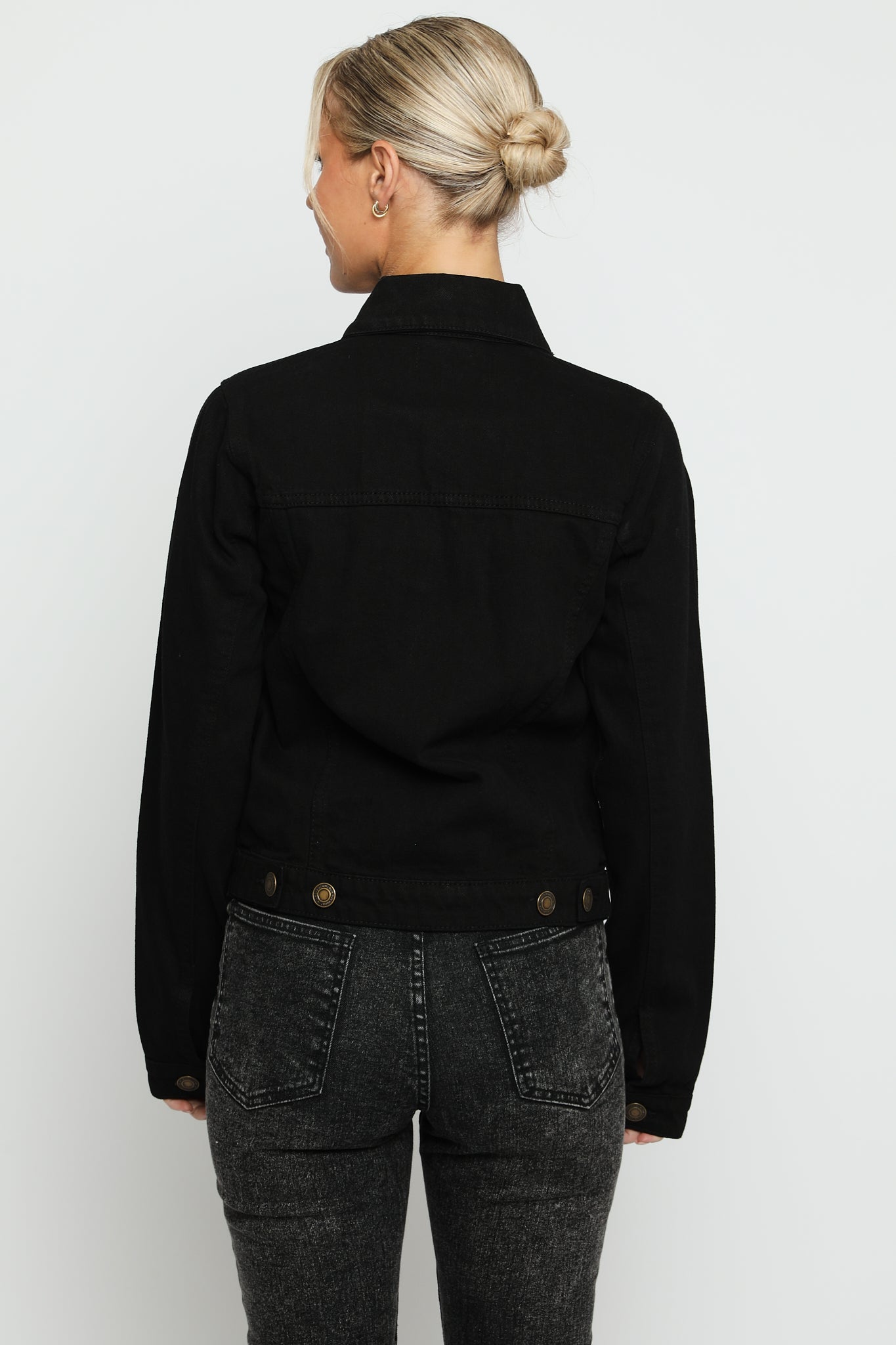 Full back view of black denim trucker jacket for women showing clean design and button detail at hem