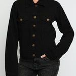 Close up of black denim jacket showing gold buttons, pointed collar, and chest pockets - women's cotton trucker jacket detail view