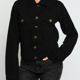 Close up of black denim jacket showing gold buttons, pointed collar, and chest pockets - women's cotton trucker jacket detail view