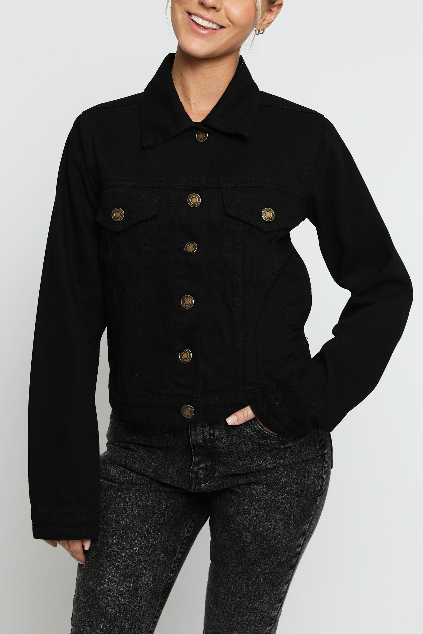 Close up of black denim jacket showing gold buttons, pointed collar, and chest pockets - women's cotton trucker jacket detail view