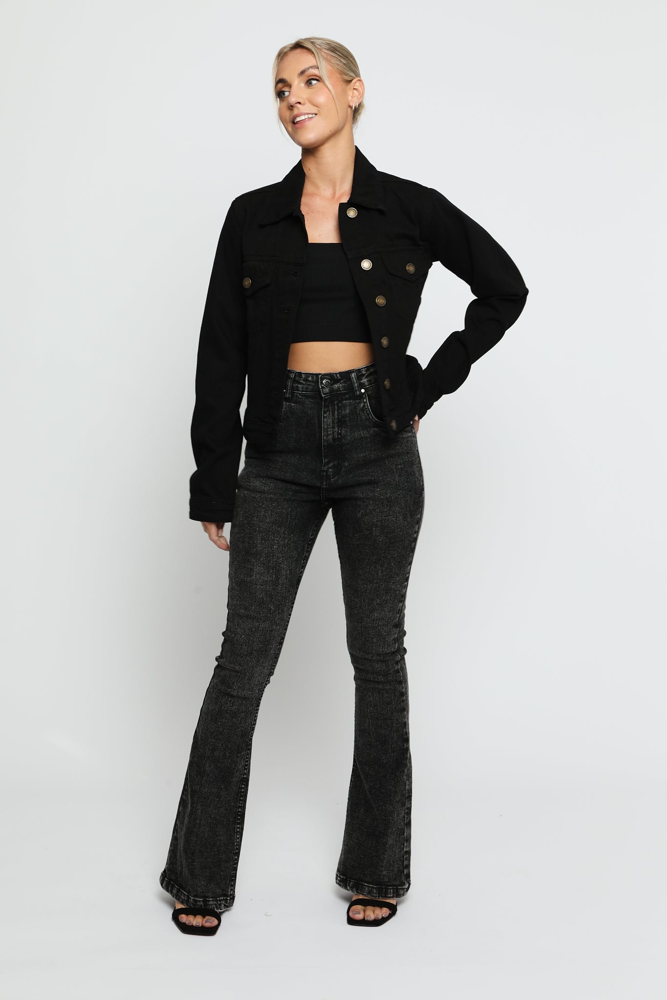 Women wearing black denim trucker jacket with hand on hip - button front cotton jacket styled with high waist flare jeans