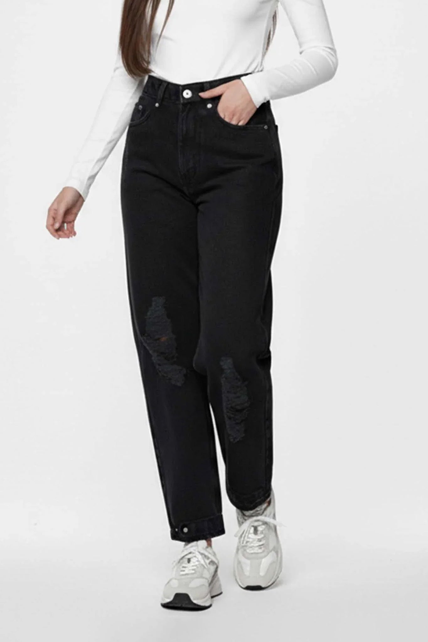 Person wearing black distressed jeans and white sneakers on a white background