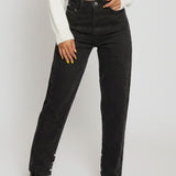 Person wearing black high-waisted jeans and a white sweater on a plain background