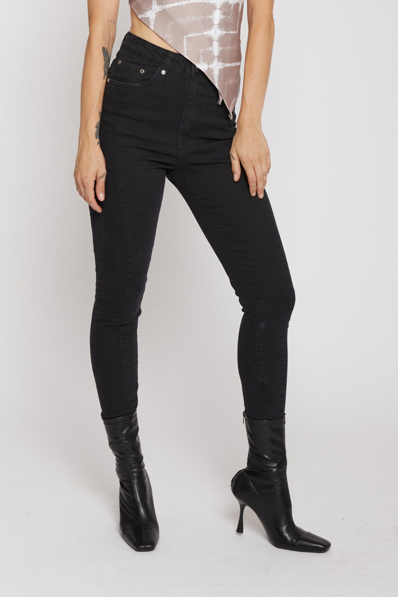 Person wearing black high-waisted jeans and black knee-high boots on a white background