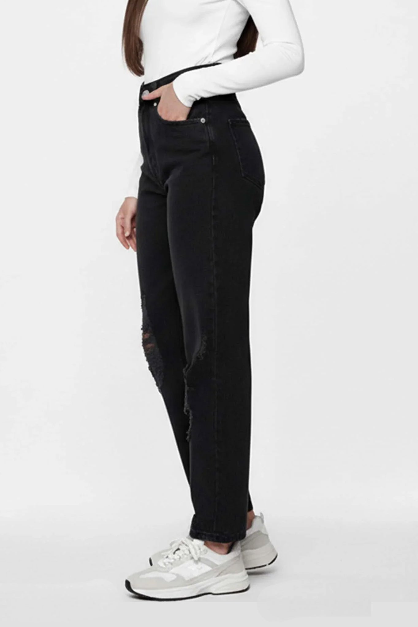 Person wearing black high-waisted jeans and white sneakers on a white background