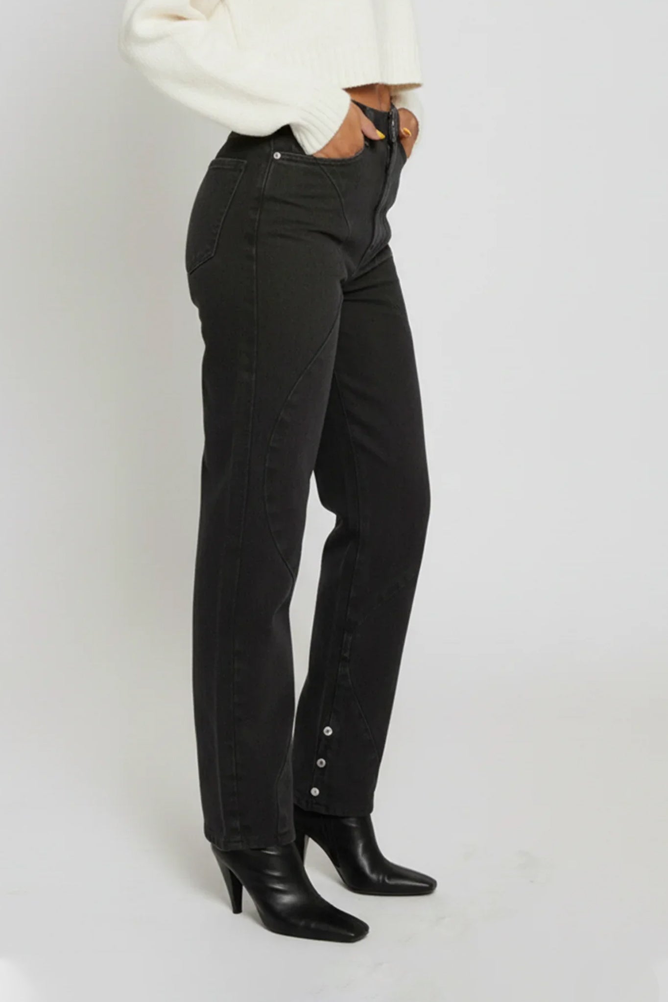 Person wearing black high-waisted jeans with button details on a white background