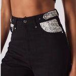 Angled close up of the high waist and embellished front pocket trim on black jeans