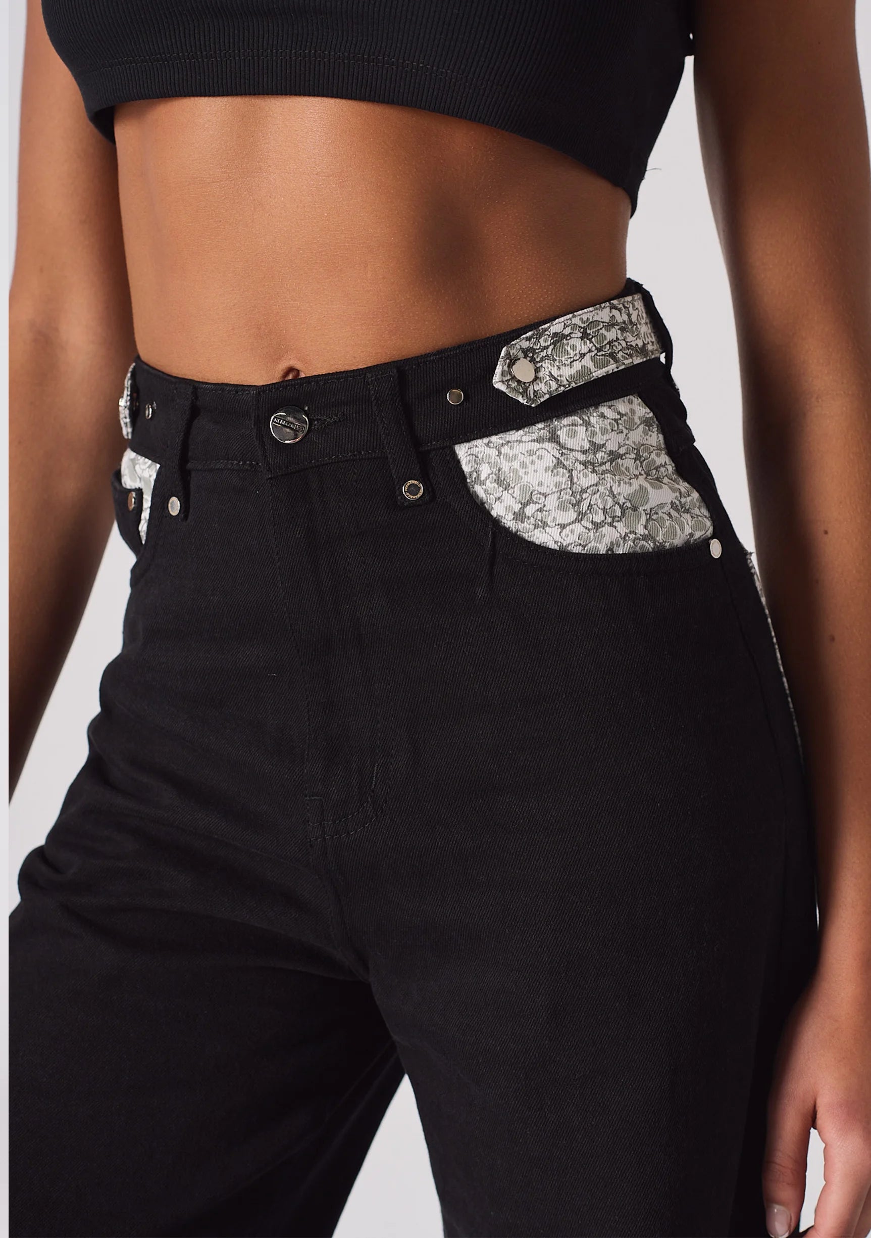 Angled close up of the high waist and embellished front pocket trim on black jeans