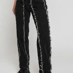 Black jeans with distressed details worn by a person on a white background