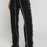 Black jeans with distressed details worn by a person on a white background