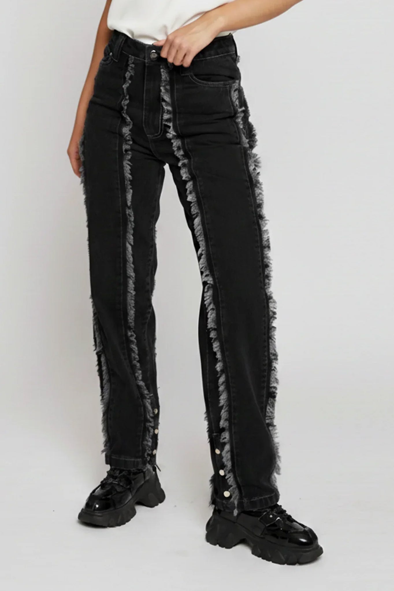 Black jeans with distressed details worn by a person on a white background