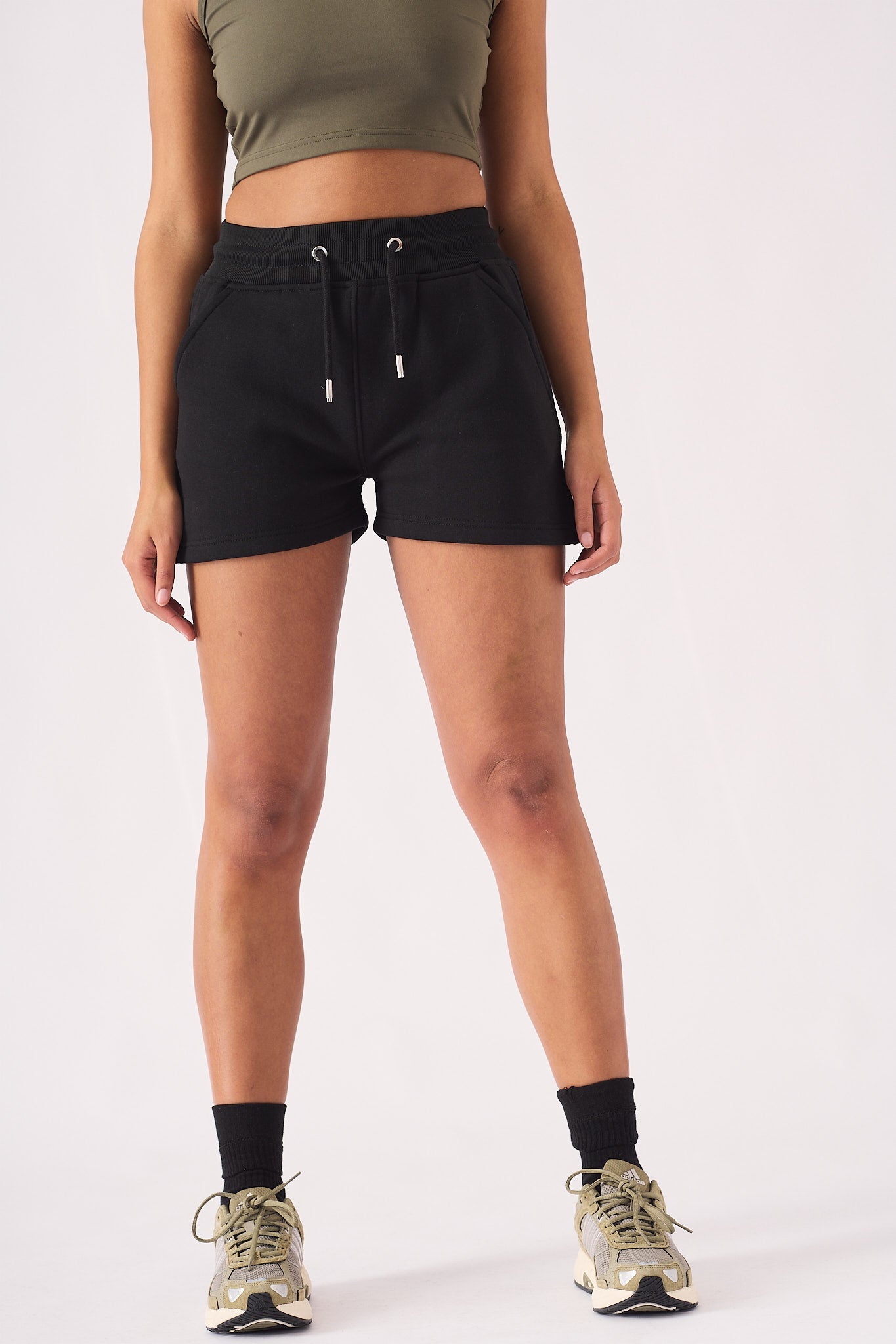 Full length front view of a woman in black jogger shorts and a green cap