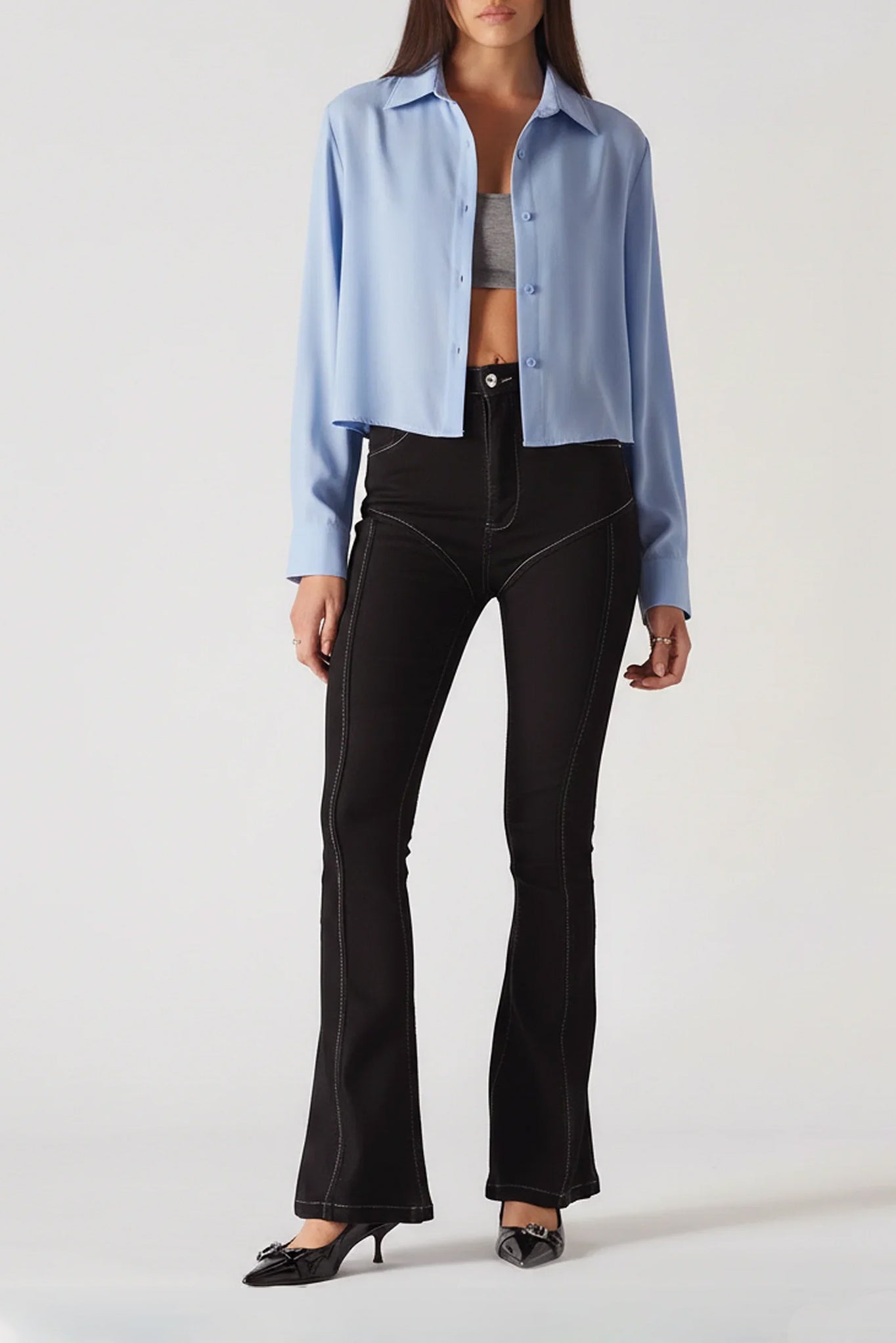 Person wearing a light blue shirt, gray top, and black pants on a white background