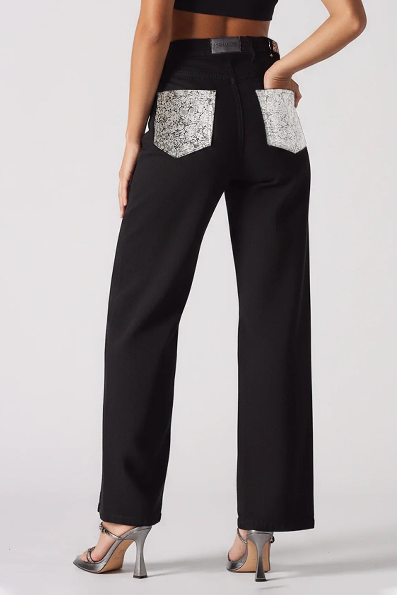 Black pants with silver pocket designs worn by a person on a white background