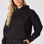 A woman posing in a black pullover hoodie with a chest logo