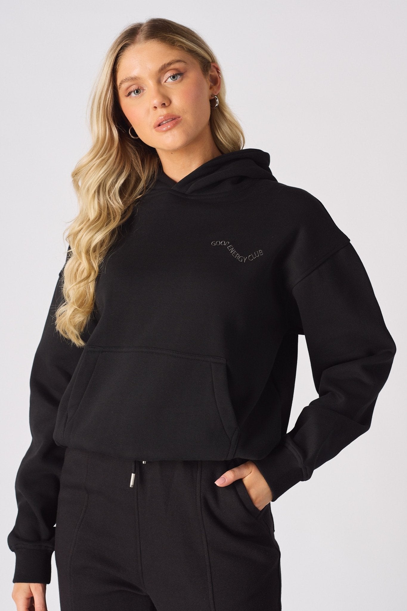 A woman posing in a black pullover hoodie with a chest logo