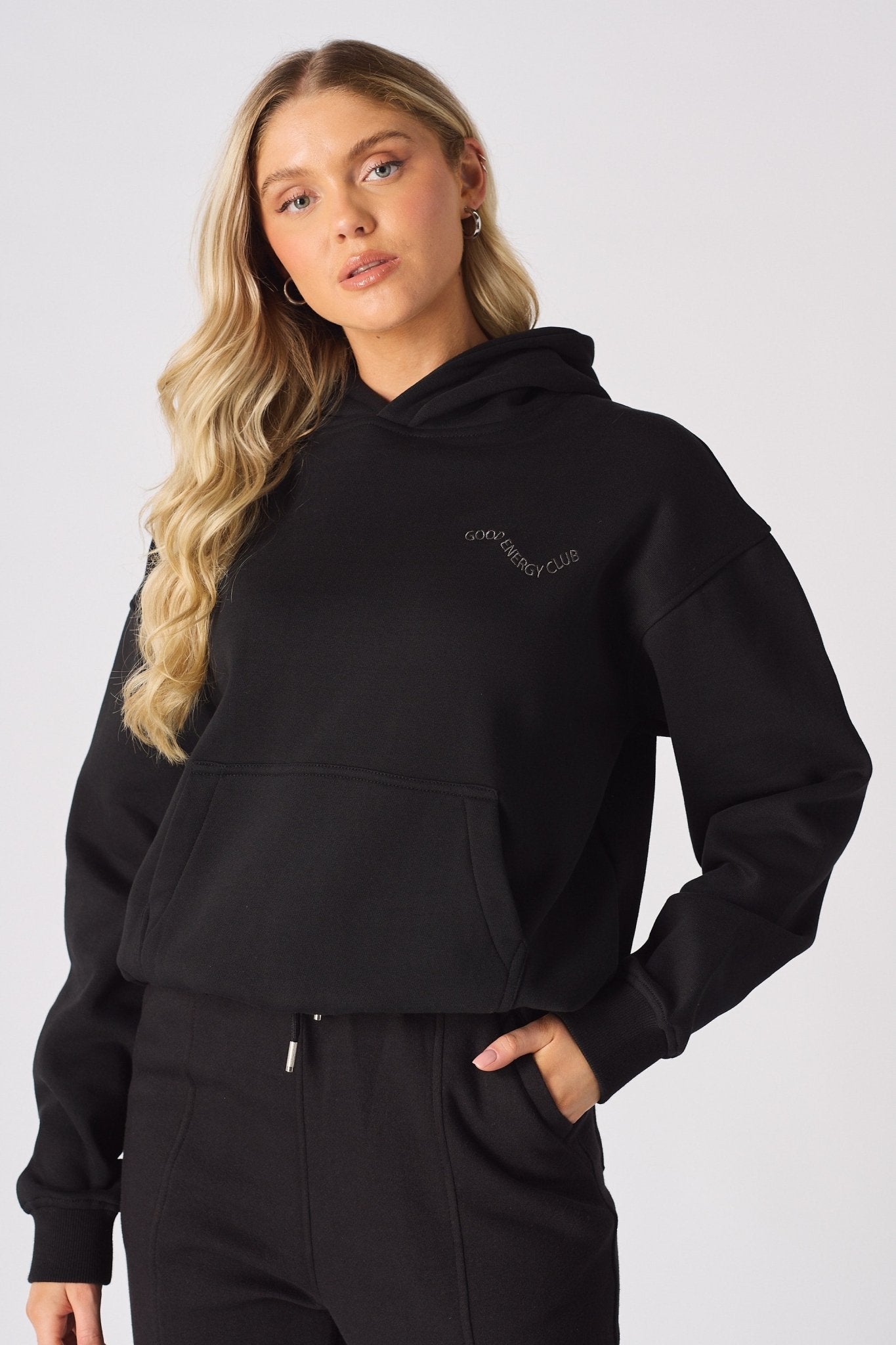 A woman posing in a black pullover hoodie with a chest logo