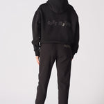 A model wearing a black pullover hoodie with hands on hips