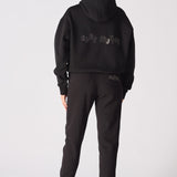 A model wearing a black pullover hoodie with hands on hips
