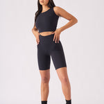 A full front view of a woman wearing a black racer neck crop top and matching shorts with a cap