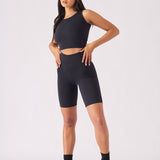 A full front view of a woman wearing a black racer neck crop top and matching shorts with a cap