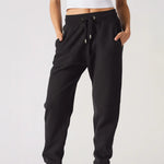 A woman wearing black relaxed fit joggers womens standing against a plain background.