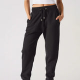 A woman wearing black relaxed fit joggers womens standing against a plain background.