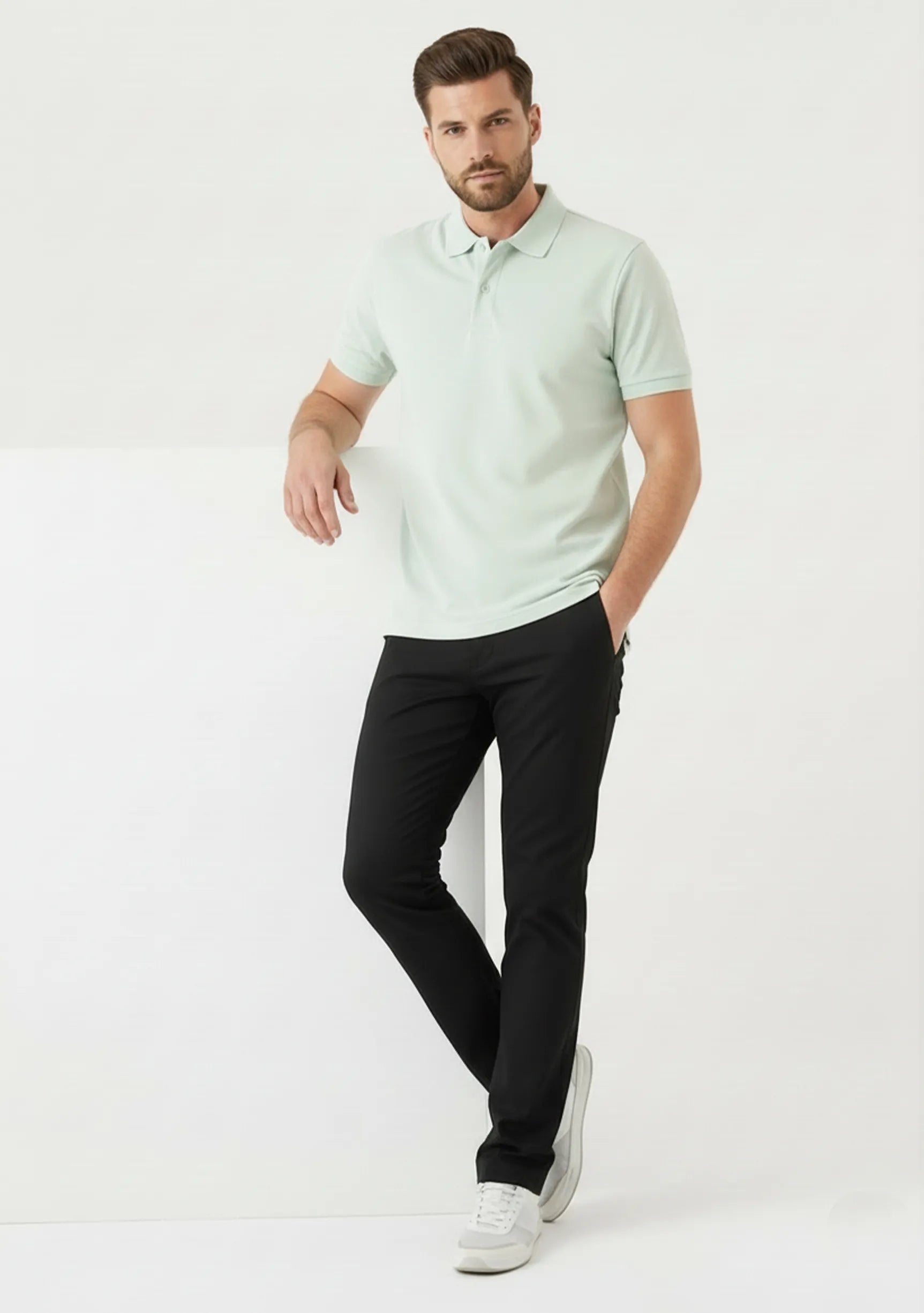 Man leaning against a white prop wearing Jmojo black slim fit trousers.