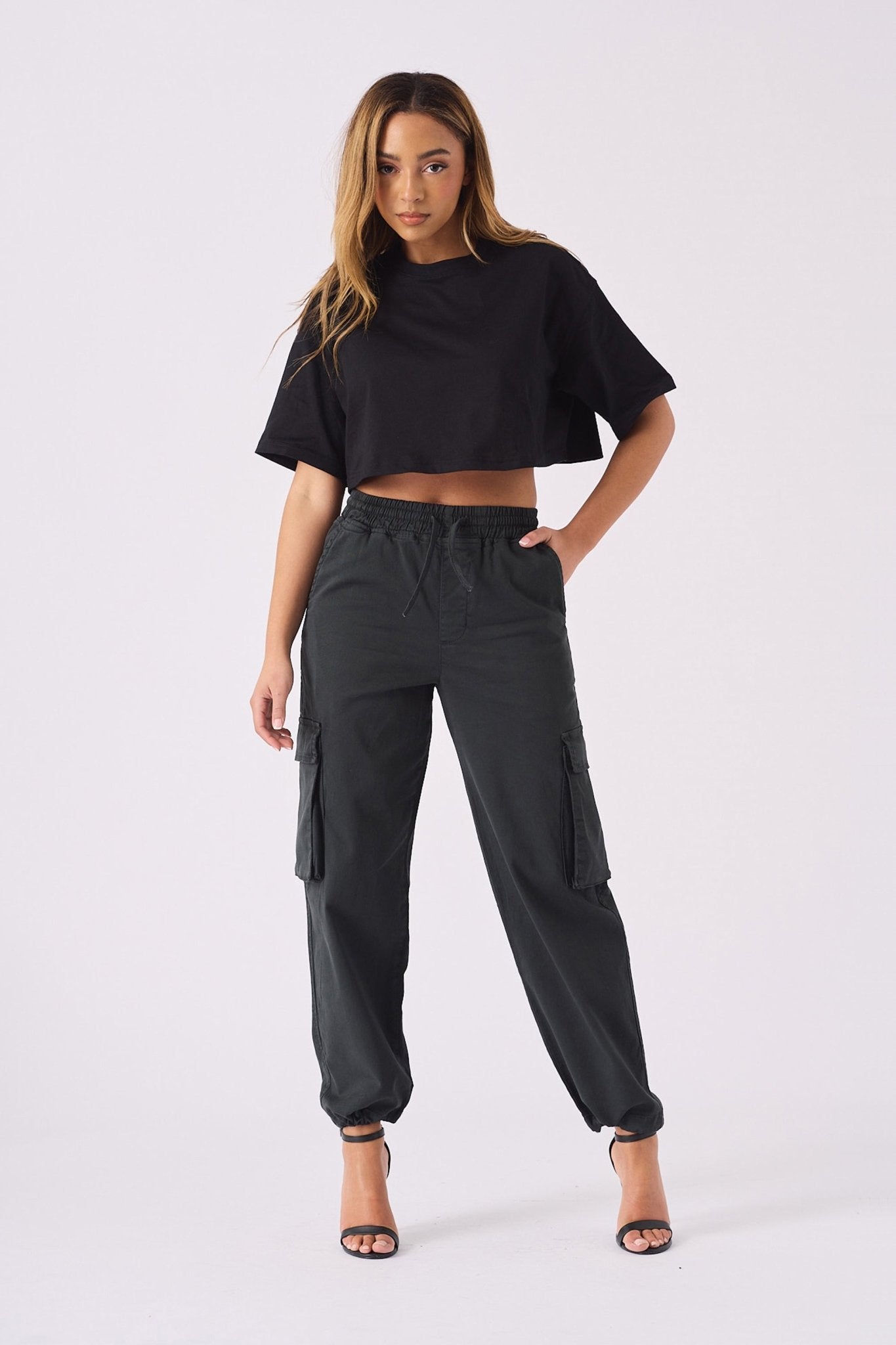 A woman posing in black straight leg cargo pants women's with a matching black crop top.