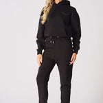 Full body view of a model posing in black tapered joggers womens and trainers.